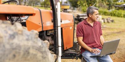 Man sitting on tractor on rural farm with laptop